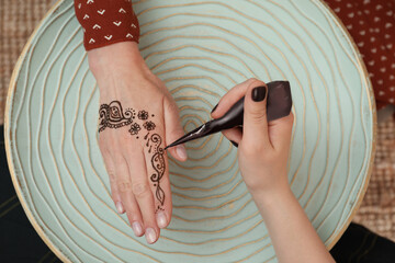 Wall Mural - Professional mehndi master making henna tattoo at table, top view