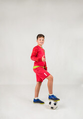 a happy young football player in a red uniform plays with a soccer ball on a white background with a place for text