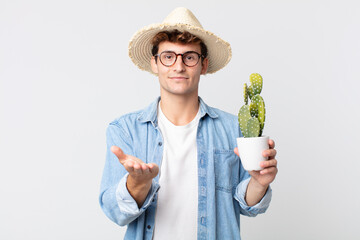 Wall Mural - young handsome man smiling happily with friendly and  offering and showing a concept. farmer holding a decorative cactus