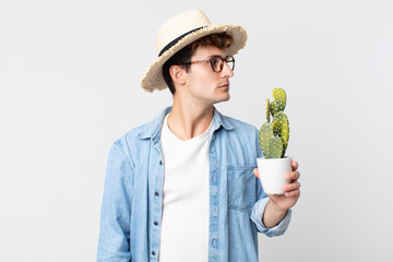 Wall Mural - young handsome man on profile view thinking, imagining or daydreaming. farmer holding a decorative cactus