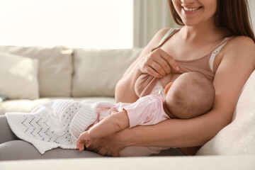 Poster - Young woman breastfeeding her little baby on sofa at home, closeup