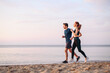© ViDi Studio - Full body side view couple young two friends strong sporty sportswoman sportsman woman man in sport clothes warm up training run on sand sea ocean beach outdoor jog on seaside in summer day morning.