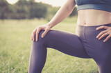 Fototapeta Las - Part of body of a woman athlete. A woman stretches her legs before training. The athlete is doing stretching in nature. Yoga class