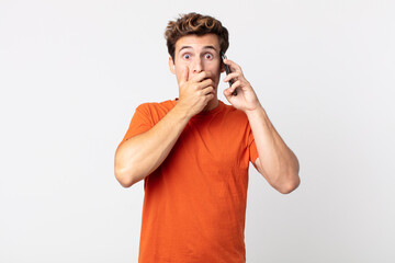 Wall Mural - young handsome man covering mouth with hands with a shocked and talking with a smart phone