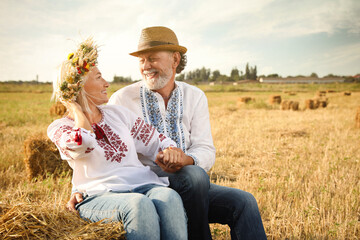 Poster - Happy mature couple wearing Ukrainian national clothes on hay bale in field