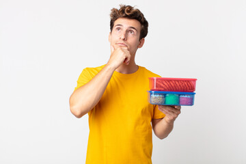 Wall Mural - young handsome man thinking, feeling doubtful and confused and holding lunch boxes