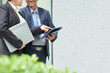 © DragonImages - Smiling senior entrepreneurs standing outdoors and discussing data on digital tablet