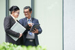 © DragonImages - Smiling senior entrepreneur showing contract or article on tablet computer to colleague when they are standing on the street