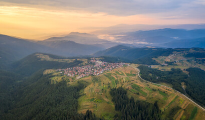 Wall Mural - aerial view of picturesque green mountain slopes and a small village nestled in them in golden hour 