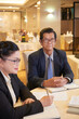 © DragonImages - Portrait of serious senior businessman sitting at restaurant table with business partner and writing in planner
