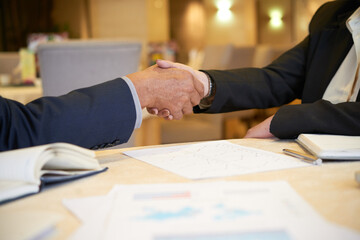 Wall Mural - Close-up image of senior entrepreneurs shaking hands after discussing reports with charts and diagrams