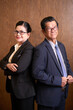 © DragonImages - Aged successful businessman and businesswoman standing back to back and looking at camera