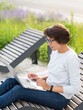 © Konstantin Aksenov - Woman sits with laptop on urban park bench. Freelancer at work. Student learns remotely from outdoors. Modern lifestyle.