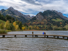 Autumn, Couple Sitting On The Shore Lake Schwarzsee And Admire The Alpine Valley Of The Brekka Abis.