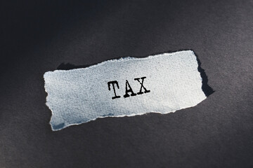 TAX - text on torn paper on dark desk in sunlight.