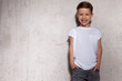 © deniskomarov - Happy laughing cool little boy in white t-shirt posing on background of grunge concrete wall with copy space for ad. Smiling stylish fashionable schoolboy near gray wall. Children's style and fashion.