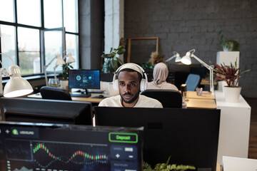 Young African businessman in headphones working in front of computer monitor in office