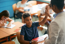African American Schoolboy And His Teacher Giving High Five In Classroom.