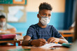 © Drazen - African American elementary student wearing protective face mask while learning in classroom at school.