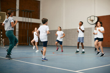 Sports teacher and group of kids exercising during physical activity class at school gym.