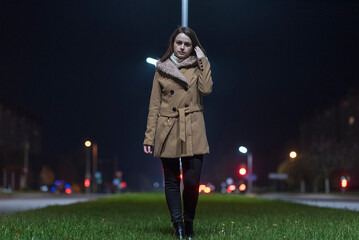 Wall Mural - Young beautiful girl in an autumn coat on the street of the night city.