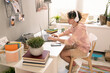 © pressmaster - Contemporary teenager sitting by table in front of laptop in domestic room