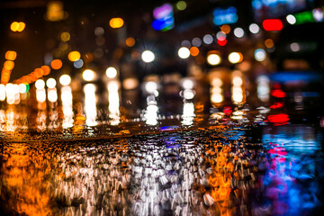 Wall Mural - Rainy night in the big city, light from the shop windows reflected on the road on which cars travel. View from the level of asphalt