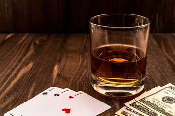 Wall Mural - Glass of whiskey and playing cards with money on the wooden table. Angle view