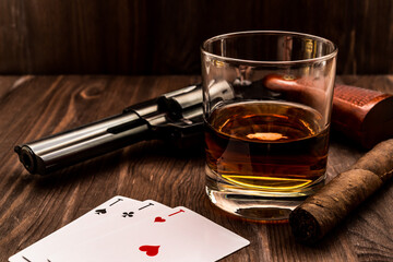 Wall Mural - Glass of whiskey and playing cards with revolver and cuban cigar on the wooden table. Angle view