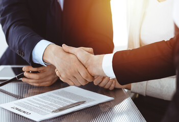 Business people shaking hands after contract signing in sunny modern office. Teamwork and handshake concept