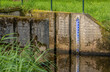 Blue enamel water level scale at the concrete exit of an old Dutch weir. Reed plants grow in the foreground. The water has a mirror-smooth surface and it reflects optimally.