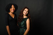 © etonastenka - Two lovely young women of different nationalities in beautiful evening dresses stand against a black background, hugging and smiling. Copy space