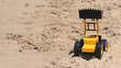 Yellow and black plastic toy bulldozer on beach sand in a sunny day