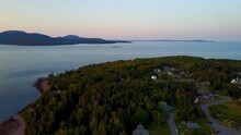 A Golden Hour Aerial Panning Drone Shot Showing Little Cranberry Island, Sutton Island, And Great Cranberry Island With Mt Desert Island In The Background  And A Lobster Boat Approaching The Harbor.