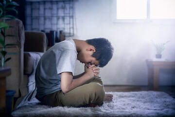 Wall Mural - Boy sitting and praying in home beside the sofa.