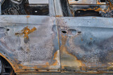Fototapeta  - Burnt-out rusty cars on a city street, vandalism. Setting fire to cars by vandals and damage to property