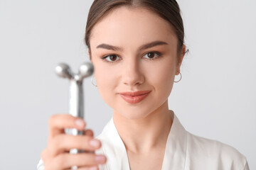 Wall Mural - Beautiful young woman with facial massage tool on light background