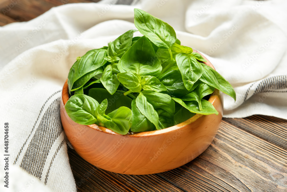 Bowl with fresh basil leaves on wooden background, closeup