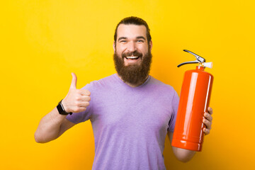 A happy young bearded man is holding a extinguisher and smiling at the camera is holding a thumb up