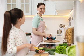 Canvas Print - Mother and daughter peeling vegetables at kitchen counter