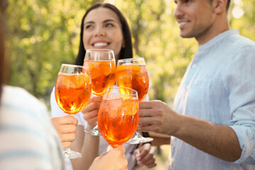 Wall Mural - Friends clinking glasses of Aperol spritz cocktails outdoors, focus on hands