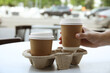 © New Africa - Woman taking paper coffee cup from cardboard holder at table outdoors, closeup
