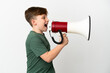 Little redhead boy isolated on white background shouting through a megaphone to announce something in lateral position