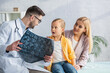 © LIGHTFIELD STUDIOS - Pediatrician holding blurred mri scan near amazed kid and mother