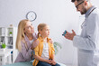 © LIGHTFIELD STUDIOS - Smiling mother hugging child near family doctor with inhaler in clinic
