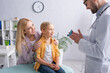 © LIGHTFIELD STUDIOS - Pediatrician holding inhaler near kid and mom in hospital