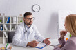 © LIGHTFIELD STUDIOS - doctor in white coat talking to blurred woman near clipboard with diagnosis