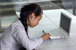 © Anna - Asian teen girl in school uniform writes in a notebook in front of a laptop