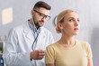 © LIGHTFIELD STUDIOS - doctor in eyeglasses examining blonde woman with stethoscope