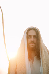 Wall Mural - Jesus Christ with staff stands in white robe against sky at sunset.